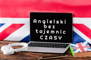 Słuchawki, słownik angielskiego oraz dwa ołówki leżące na stole z otwartym laptopem wyświetlającym napis: Angielski bez tajemnic CZASY, a w tle flaga Wielkiej Brytanii.